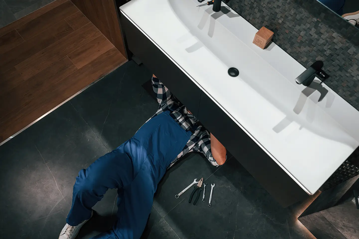 Rénovation salle de bain Bordeaux : un professionnel travaillant sous un lavabo moderne.